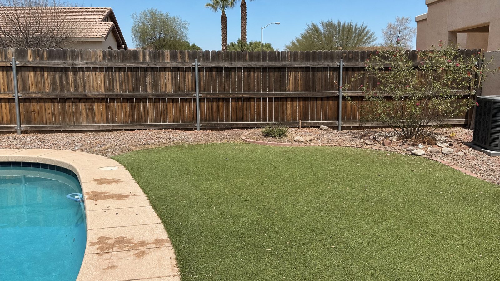 Arizona desert backyard with pool edge, artificial turf, gravel landscaping, and weathered fence