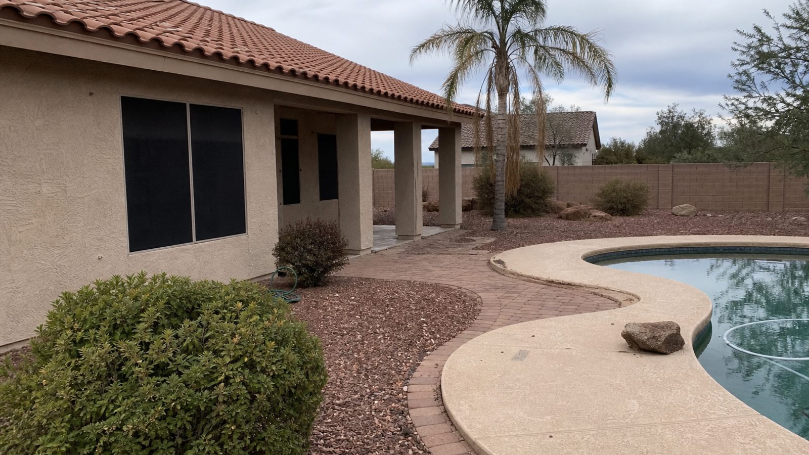 Arizona home exterior with desert landscaping, sun-faded pavers, and pool edge