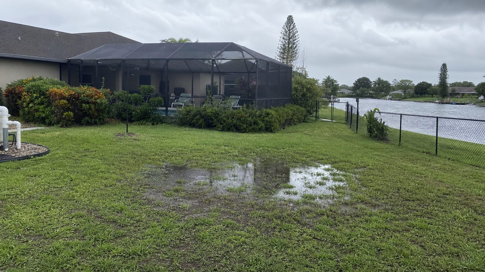 Brevard backyard near canal edge with standing water low spot, screened lanai background, storm light