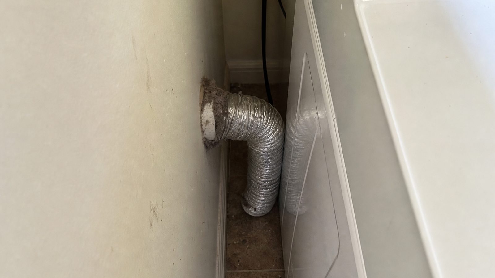 Laundry room dryer pulled slightly from wall with kinked flexible vent duct and lint at connection