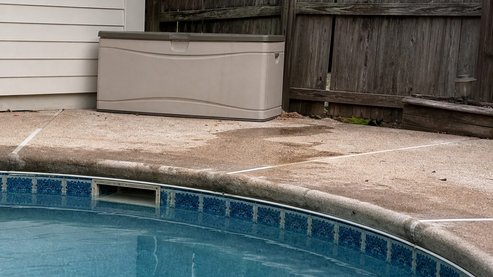 Florida residential pool deck edge near skimmer with subtle wet area and weathered coping