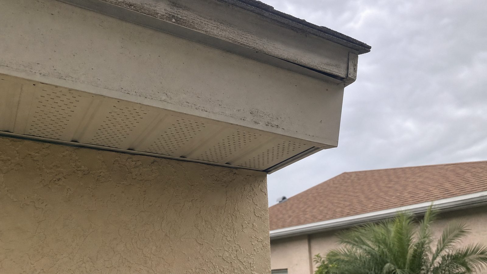 Florida stucco home soffit corner with small fascia gap and weathered paint, afternoon light