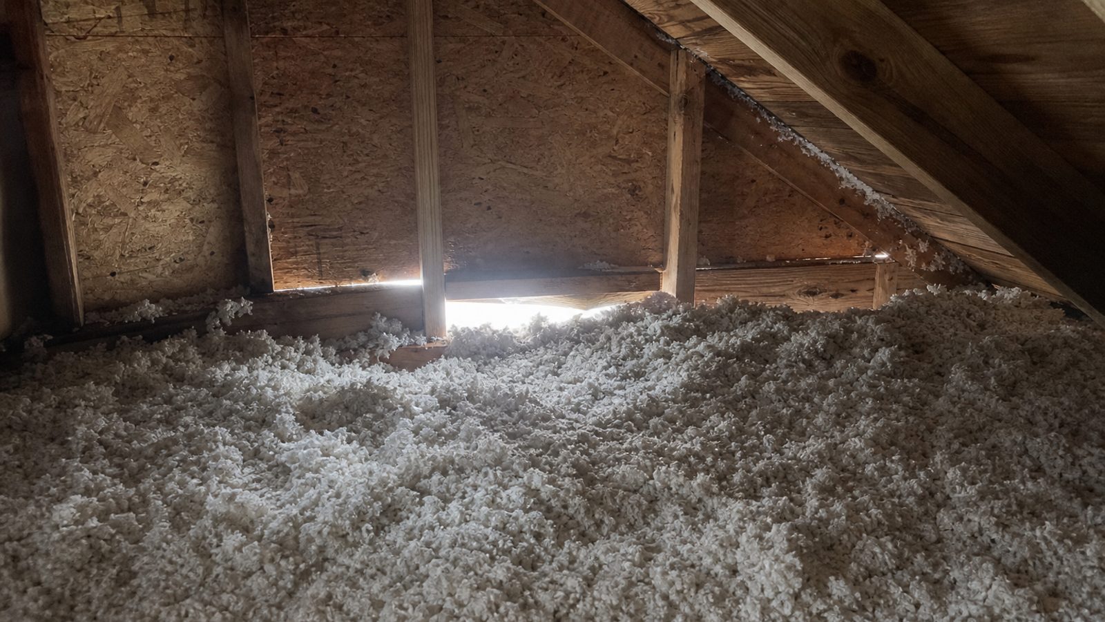 Attic access area with disturbed blown insulation near eave daylight gap, realistic residential interior